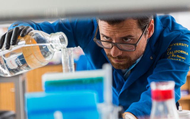 A reseaercher pouring chemicals into a beaker.