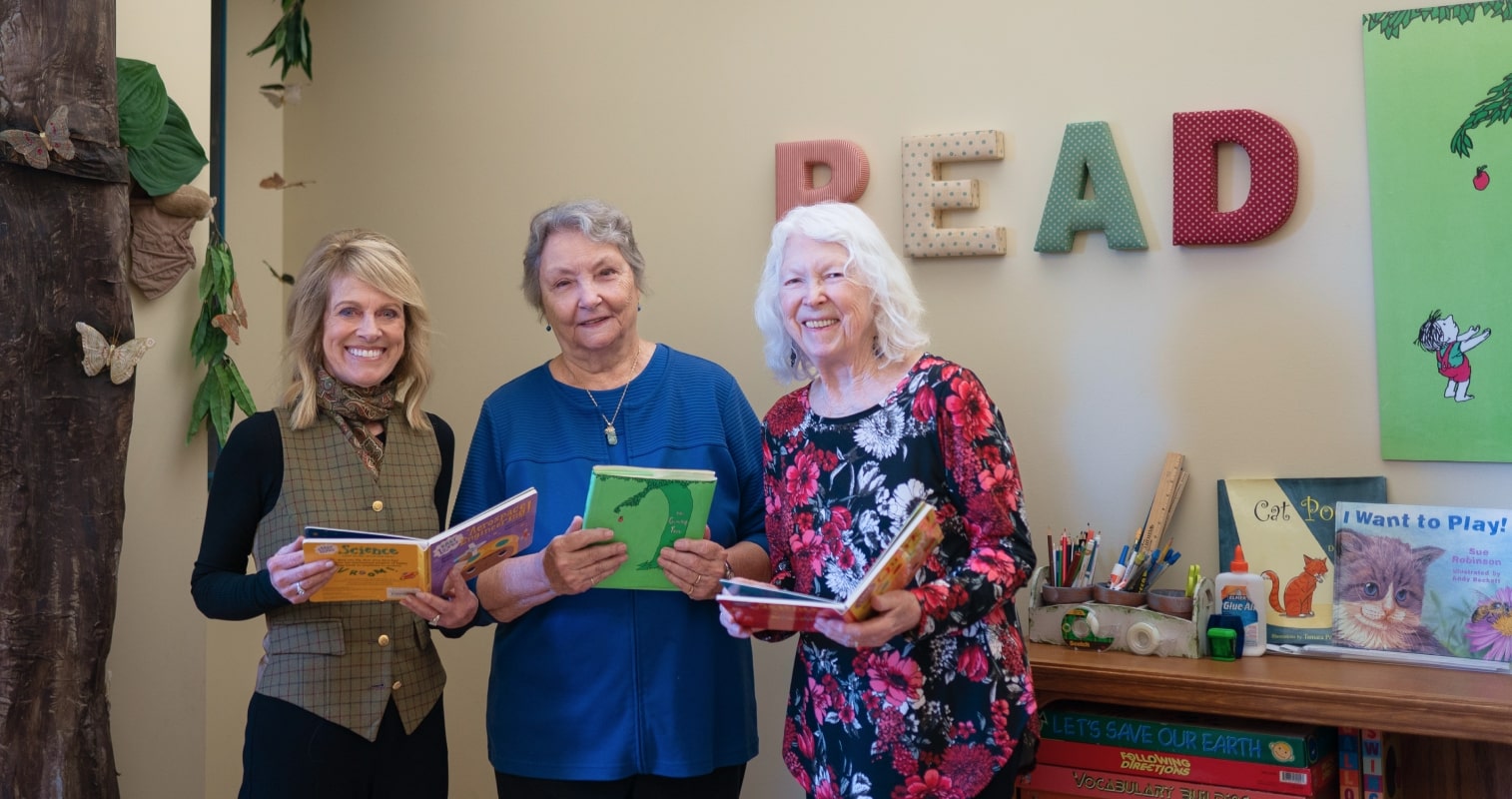 Emerita Carol Dixon, Ann Kaganoff ’75,’81 and Tina Hansen McEnroe ’89 holding books